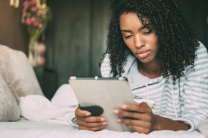 Beautiful serious thoughtful and sad black woman with curly hair using tablet on bed