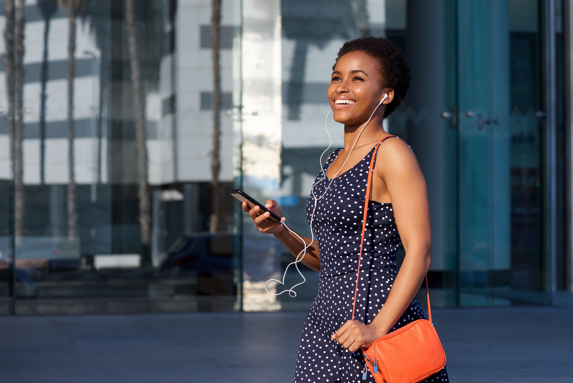 smiling young black woman walking with earphones and mobile phone